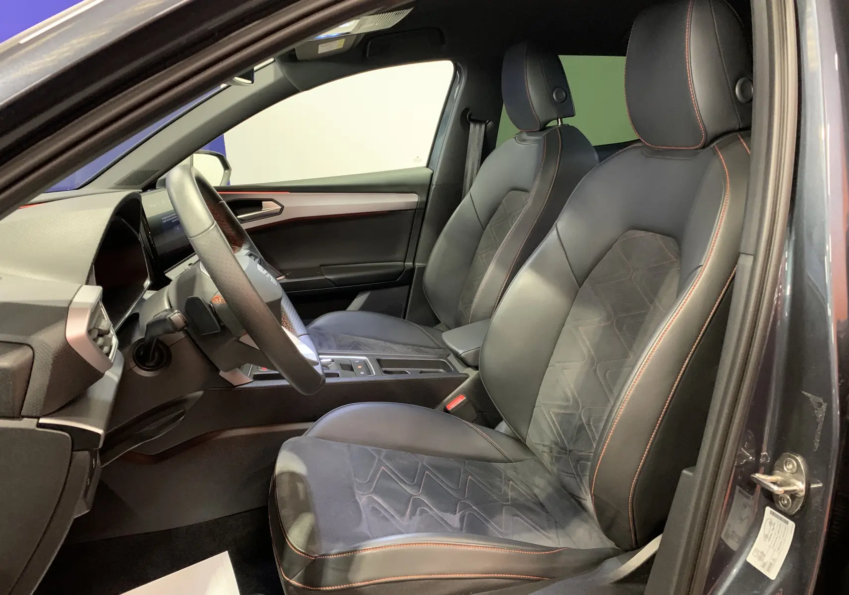 Intérieur côté conducteur d'une SEAT Leon E-HYBRID gris 2020, sièges cuir noir avec surpiqûres rouges et tableau de bord moderne.