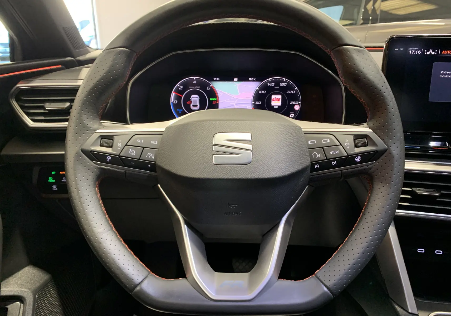 Vue rapprochée du volant perforé noir avec surpiqûres rouges du tableau de bord digital d'une SEAT LEON E-HYBRID 2020.