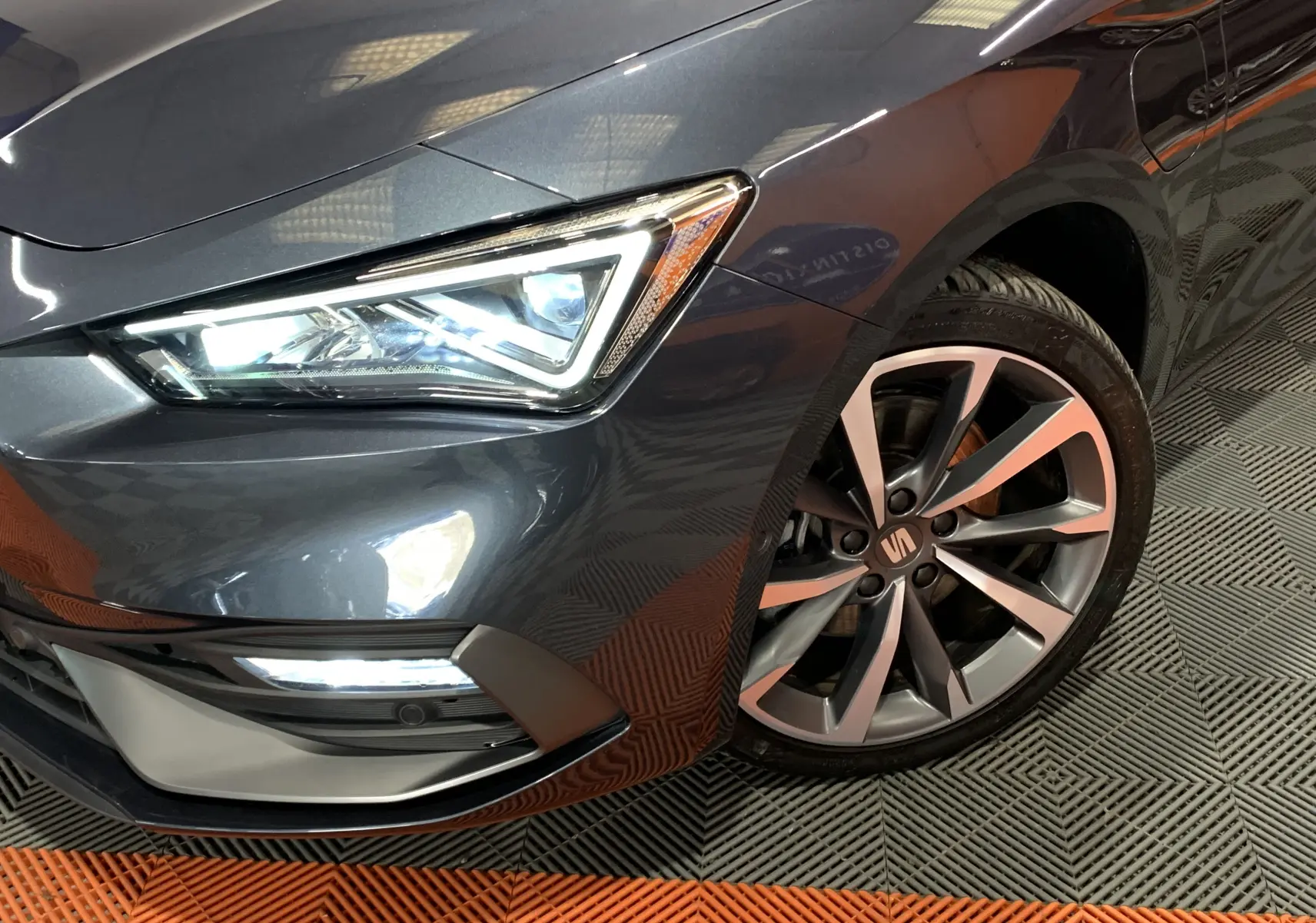 Gros plan sur l'avant droit gris métallisé d'une SEAT LEON E-HYBRID 204 FR avec phare LED et jante alliage distinctive.