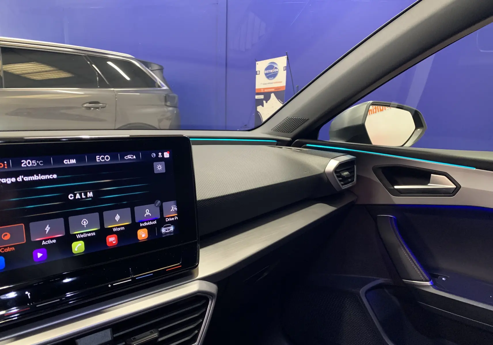 Vue intérieure côté passager de la SEAT LEON gris 2020, avec écran tactile et éclairage d'ambiance bleu.