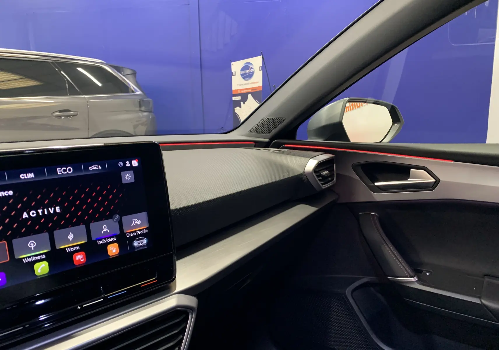 Intérieur côté passager du SEAT Leon gris 2020, tableau de bord moderne avec écran tactile et bandeau lumineux rouge.