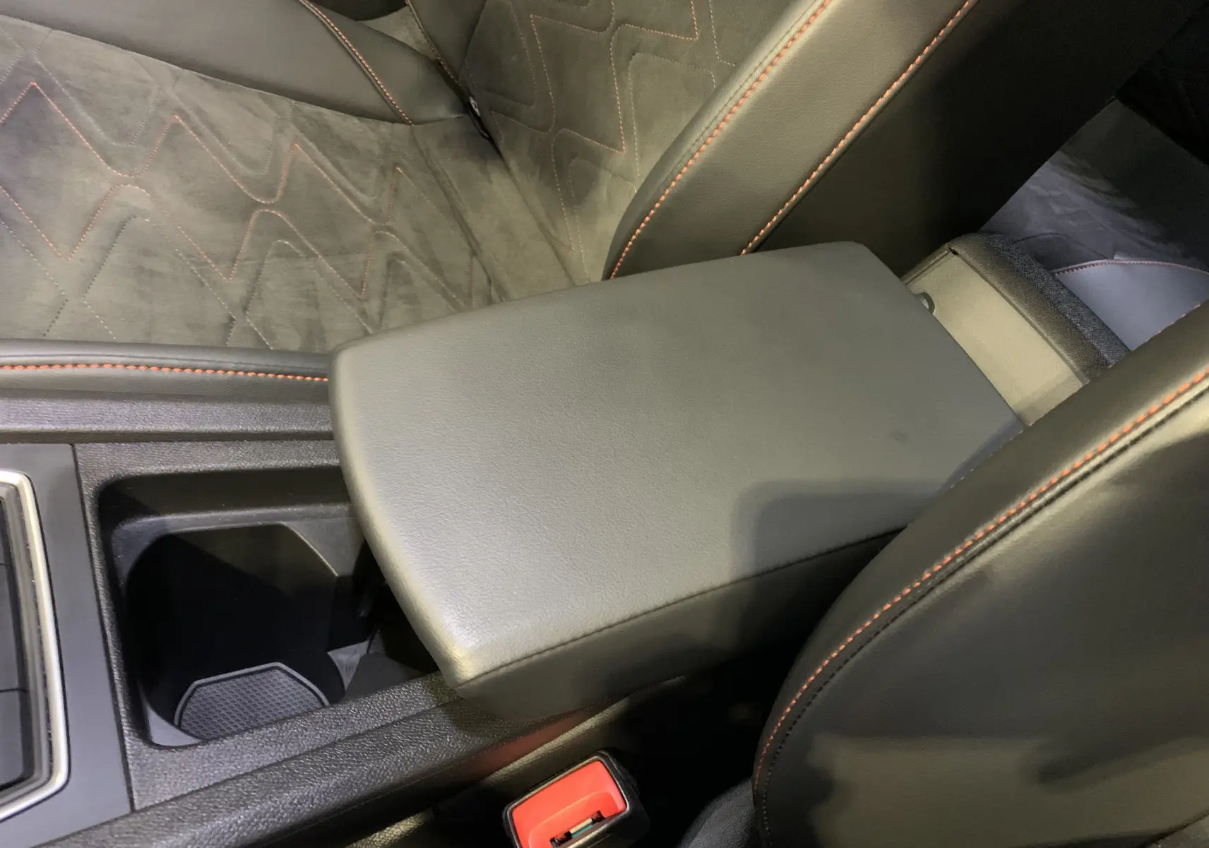 Gros plan sur l'accoudoir central noir et les sièges gris foncé avec surpiqûres orange dans la SEAT Leon E-HYBRID 2020.