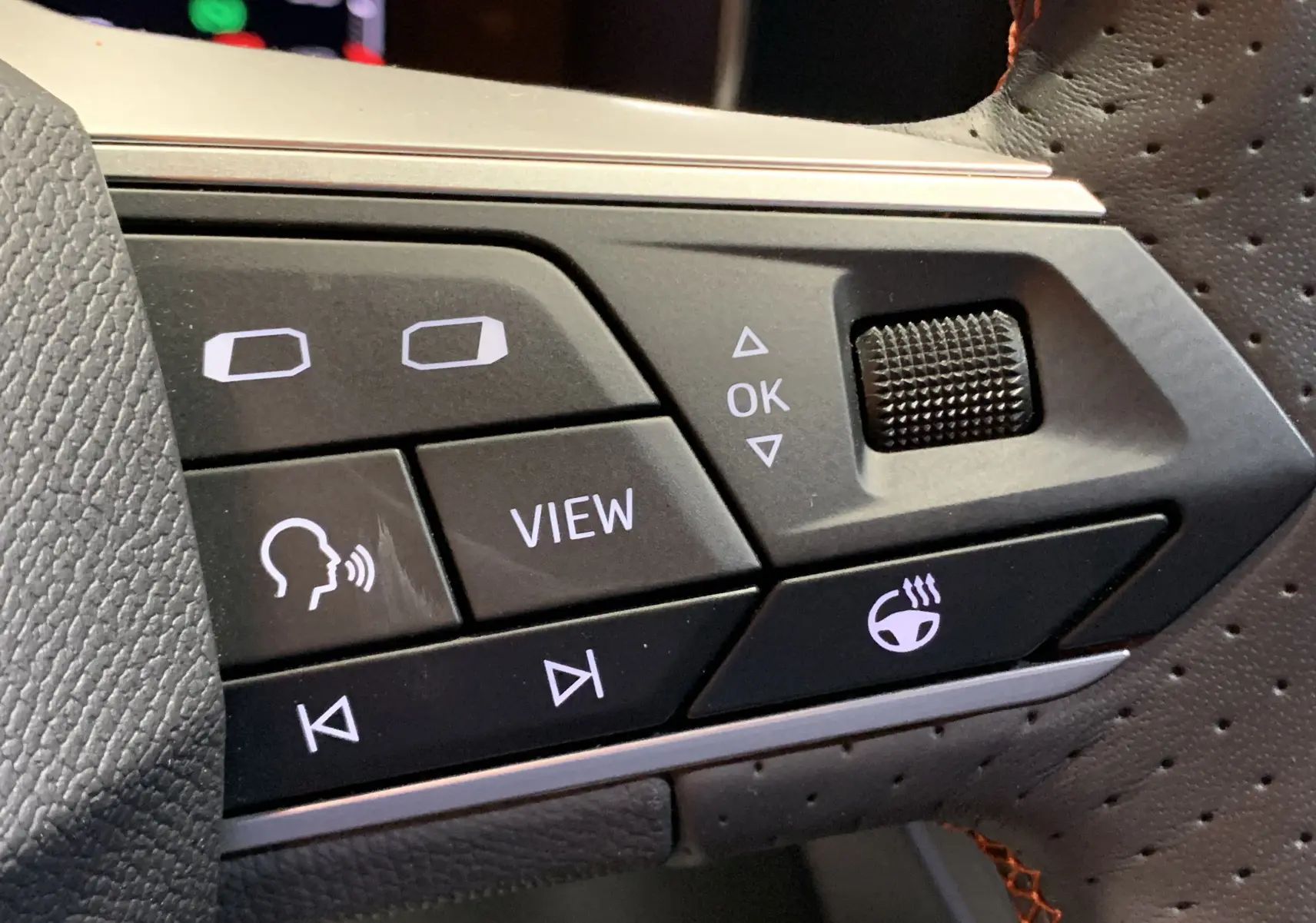 Détail des commandes noires sur le volant perforé de la SEAT LEON E-HYBRID 204 FR DSG6 gris, boutons fonctionnels éclairés.