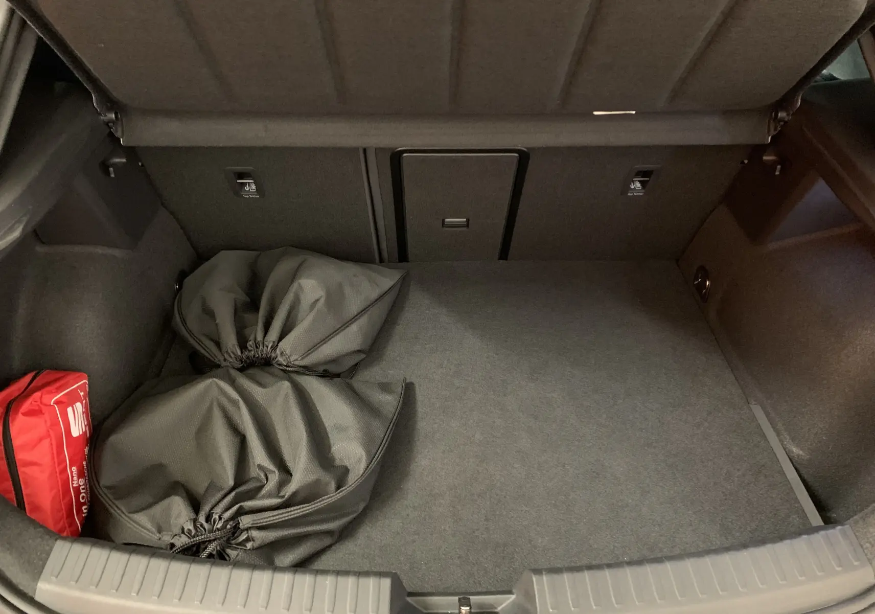 Coffre ouvert d'une SEAT LEON E-HYBRID gris 2020, vue intérieure montrant un rangement propre avec sacs et trousse de secours rouge.