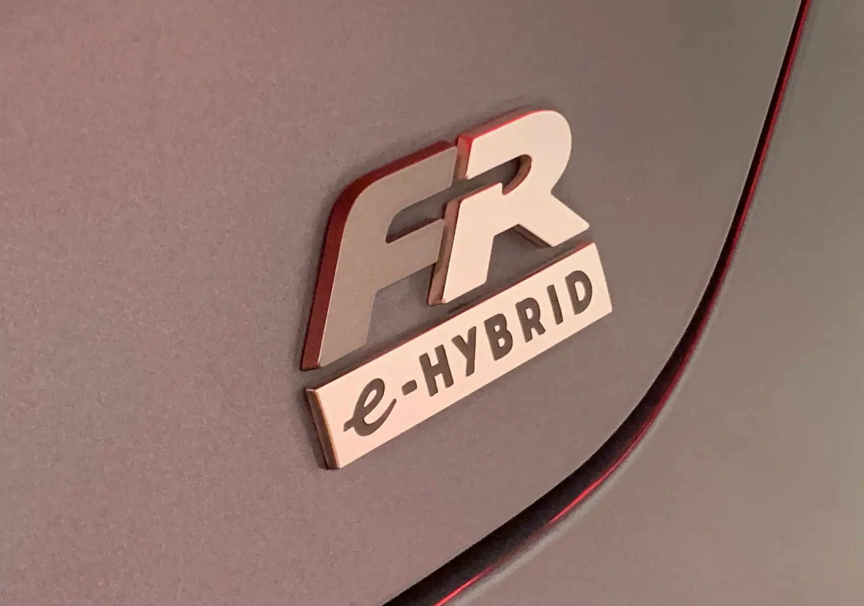 Gros plan sur l'emblème FR e-HYBRID argenté sur la carrosserie grise d'une SEAT Leon hybride.