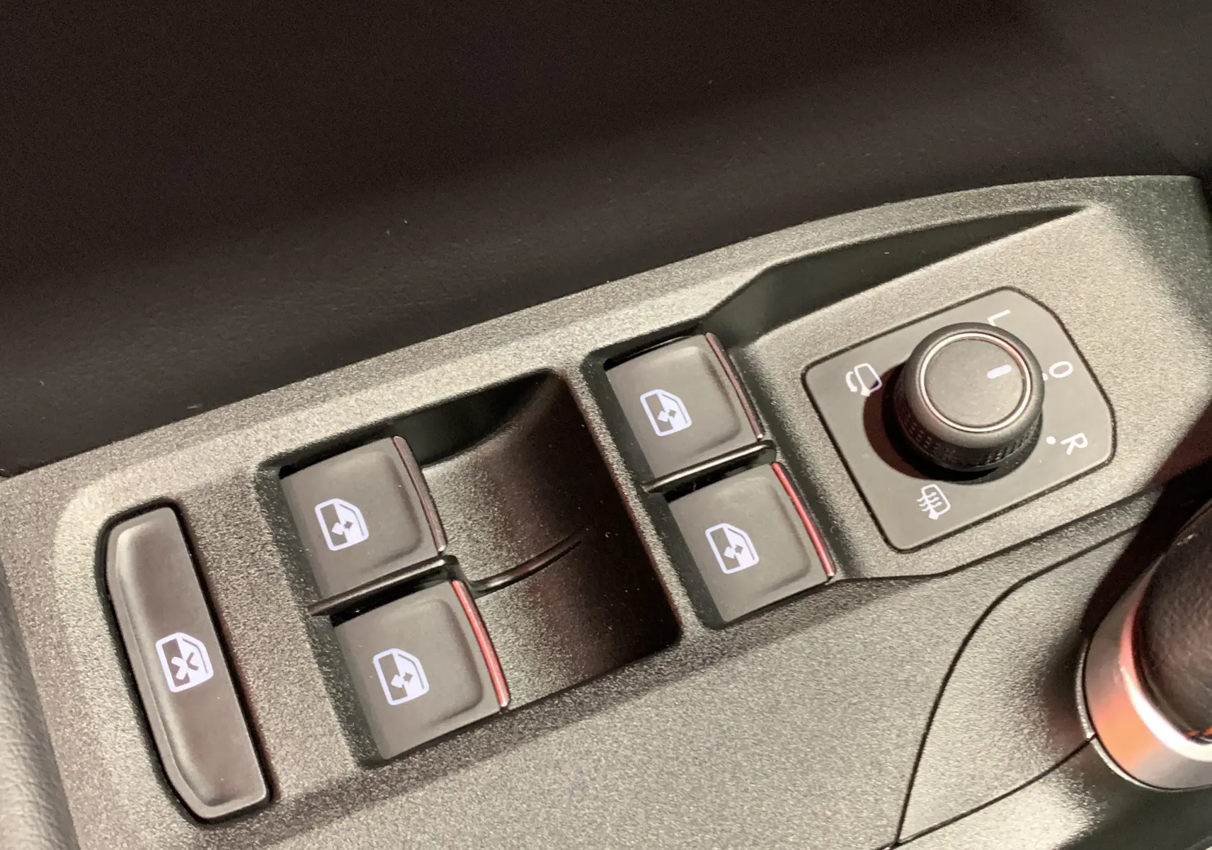 Gros plan sur les commandes de lève-vitres et réglage des rétroviseurs côté conducteur d'une SEAT Leon gris 2020.