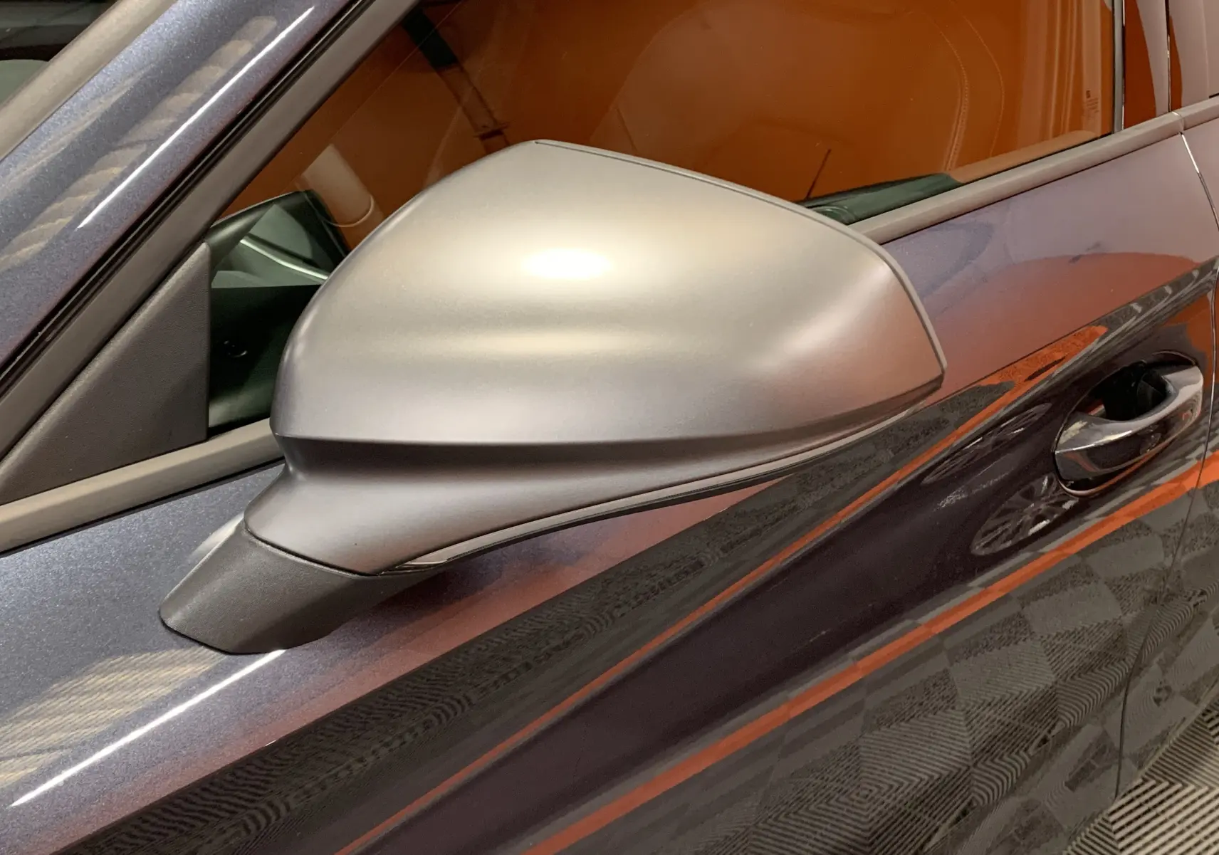 Rétroviseur côté gauche gris mat sur SEAT LEON E-HYBRID 204 FR gris, avec poignée de porte visible en arrière-plan.
