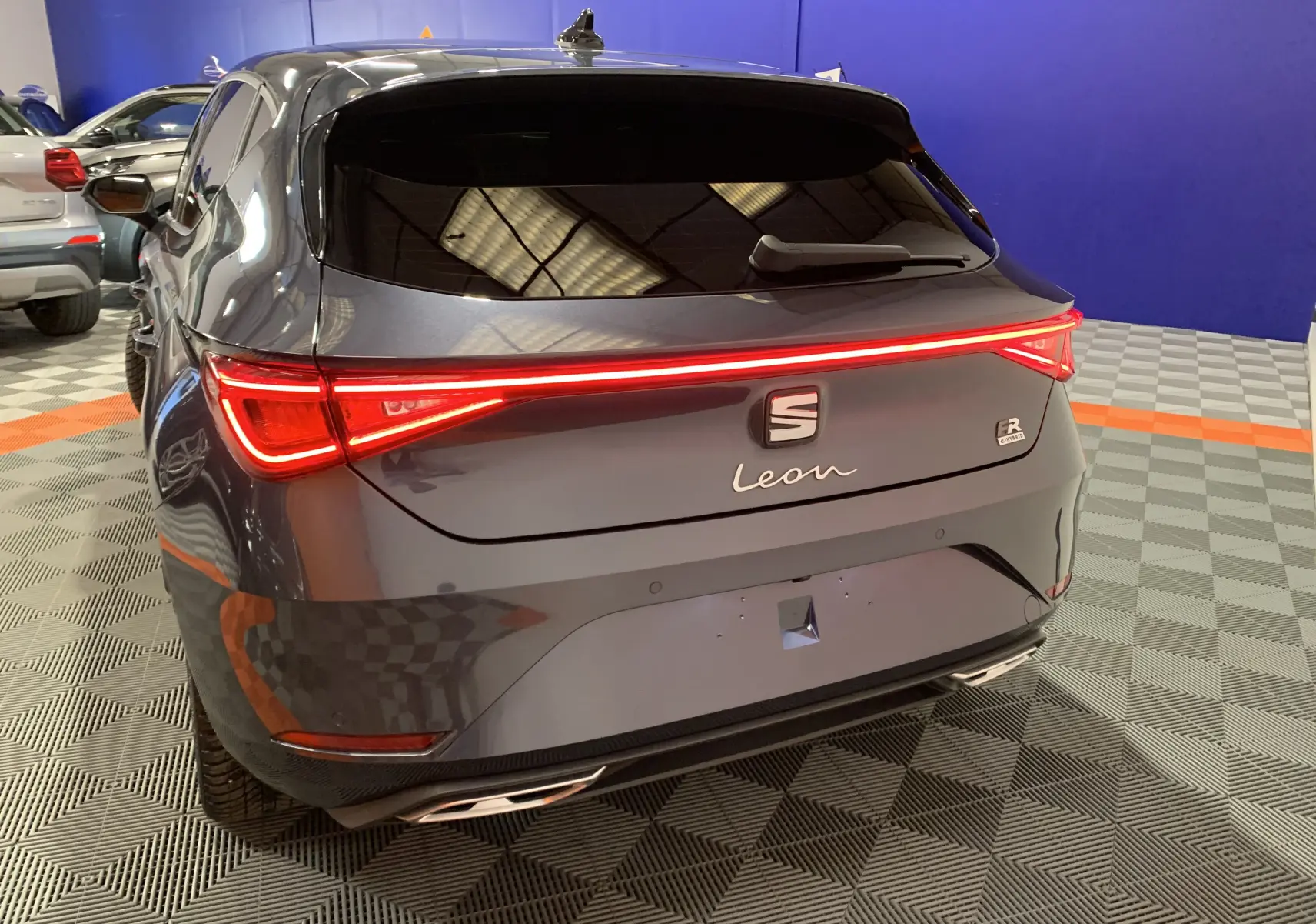 Vue 3/4 arrière d'une SEAT Leon gris métallisé avec feux LED reliés et logo FR visible sur parking intérieur.