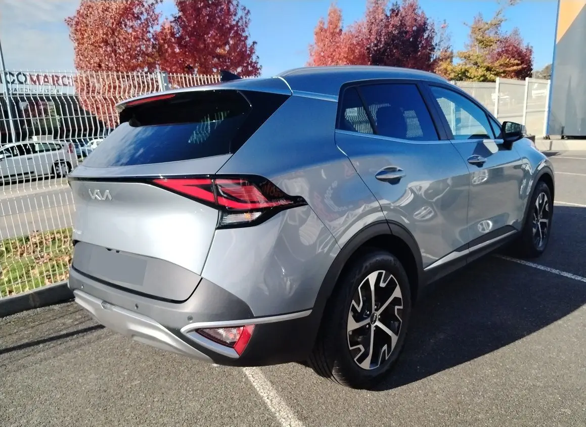 KIA SPORTAGE gris perle en 3/4 arrière droit, avec jantes bicolores et feux arrière LED distinctifs.