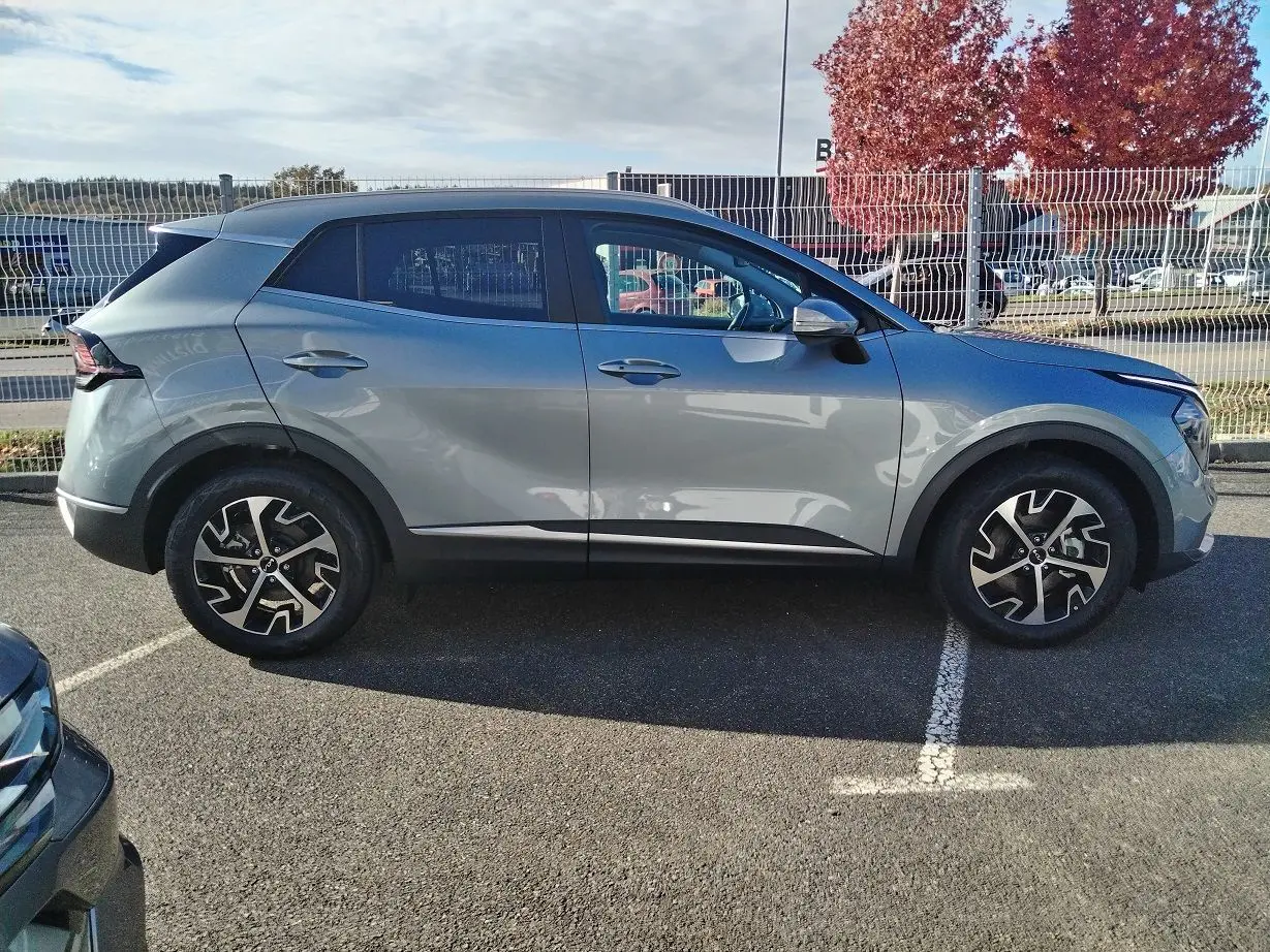 Vue de profil côté gauche du KIA Sportage gris perle 2025 avec jantes bi-ton et toit noir contrasté.