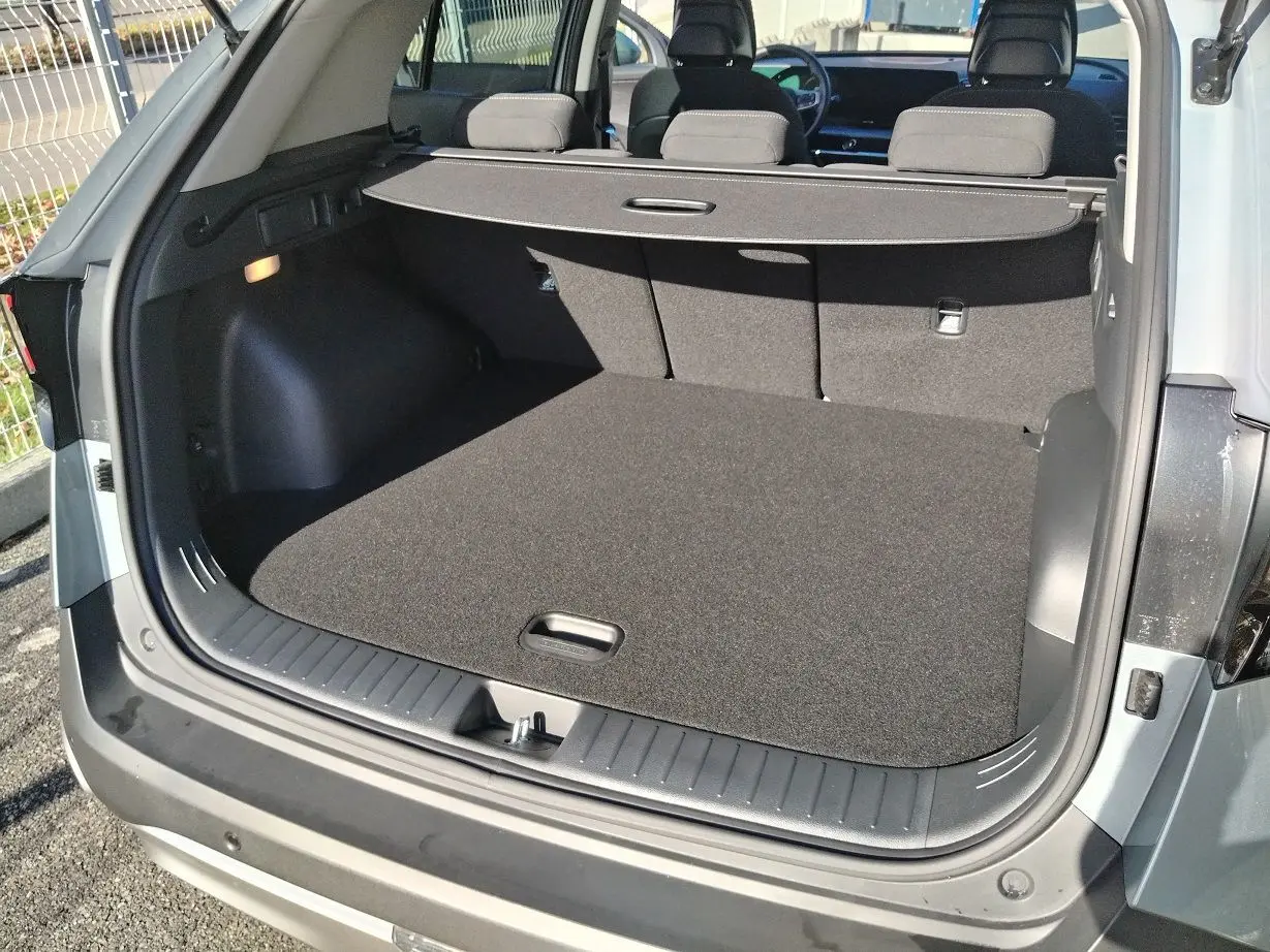 Coffre ouvert vu de l'arrière d'un KIA Sportage gris perle 2025, avec cache-bagages et intérieur noir.