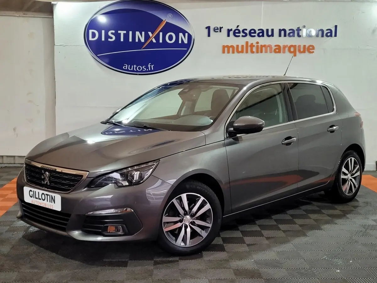 Peugeot 308 gris foncé vue 3/4 avant droit dans un showroom avec logo Distinxion en arrière-plan.