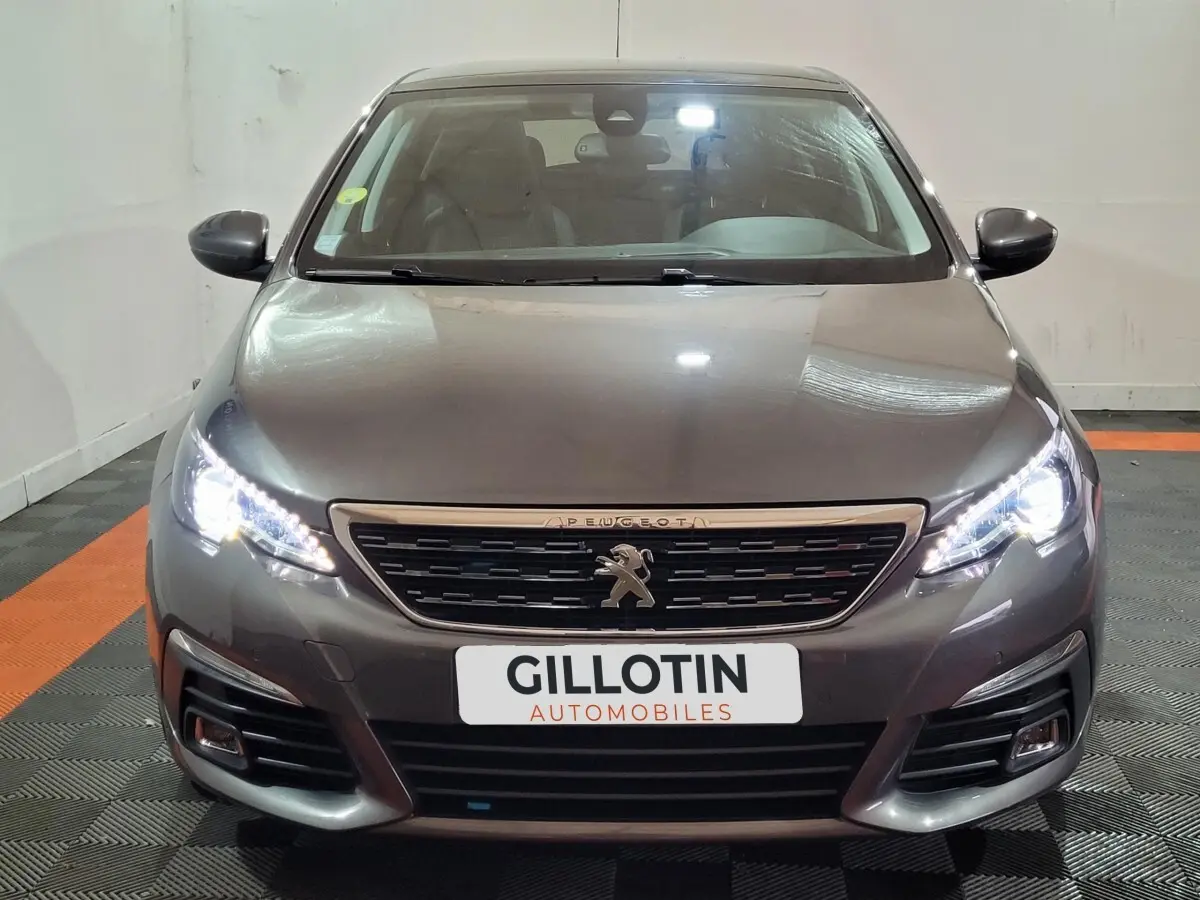 Vue frontale d'une Peugeot 308 gris foncé avec phares LED allumés et calandre distinctive au lion Peugeot.