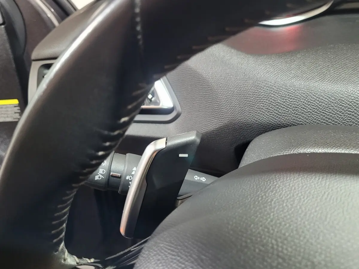 Gros plan sur la palette de changement de vitesse derrière le volant cuir noir d'une Peugeot 308 gris foncé de 2020.