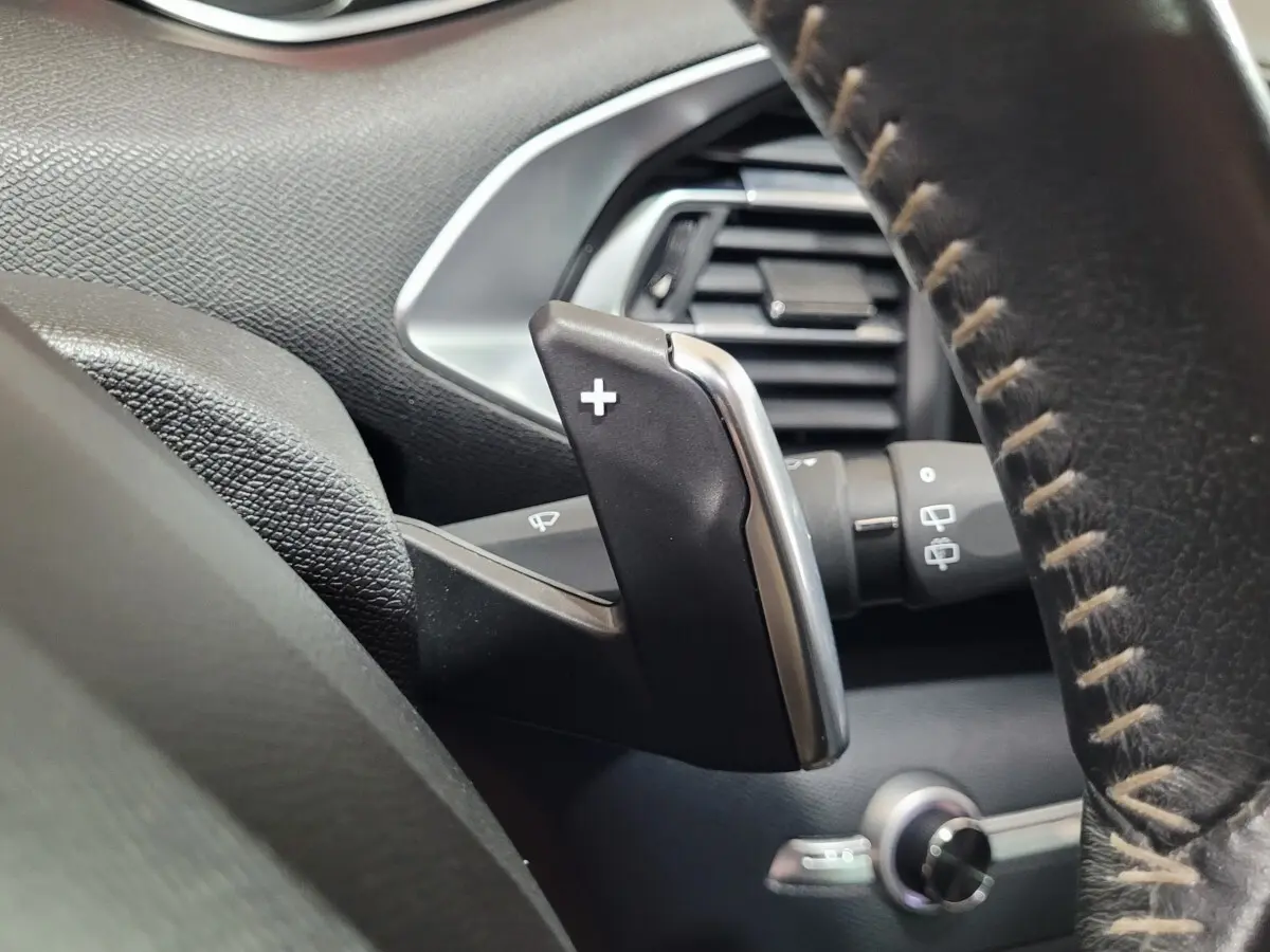 Gros plan sur la palette de changement de vitesse + au volant cuir de la Peugeot 308 gris foncé, intérieur noir.