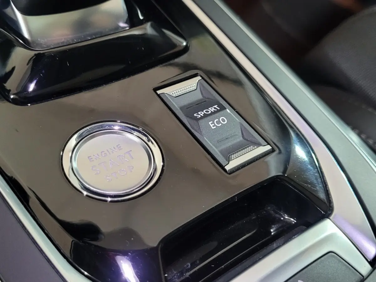 Vue rapprochée de la console centrale noire de la Peugeot 308 avec bouton démarrage et sélecteur modes Sport/Eco.