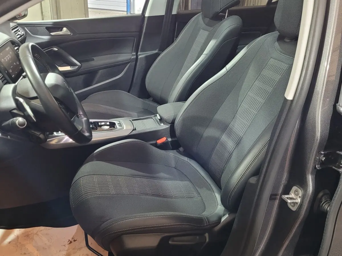Vue intérieure côté conducteur de la Peugeot 308 gris foncé, mettant en valeur les sièges avant et le volant cuir multifonctions.