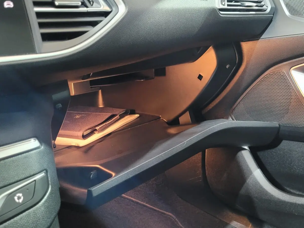 Gant de boîte à gants ouvert éclairé dans l'habitacle d'une Peugeot 308 gris foncé, côté passager.