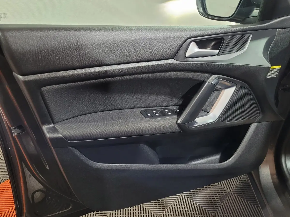 Vue rapprochée de la porte côté gauche d'une Peugeot 308 gris foncé, avec commandes électriques et poignée argentée.