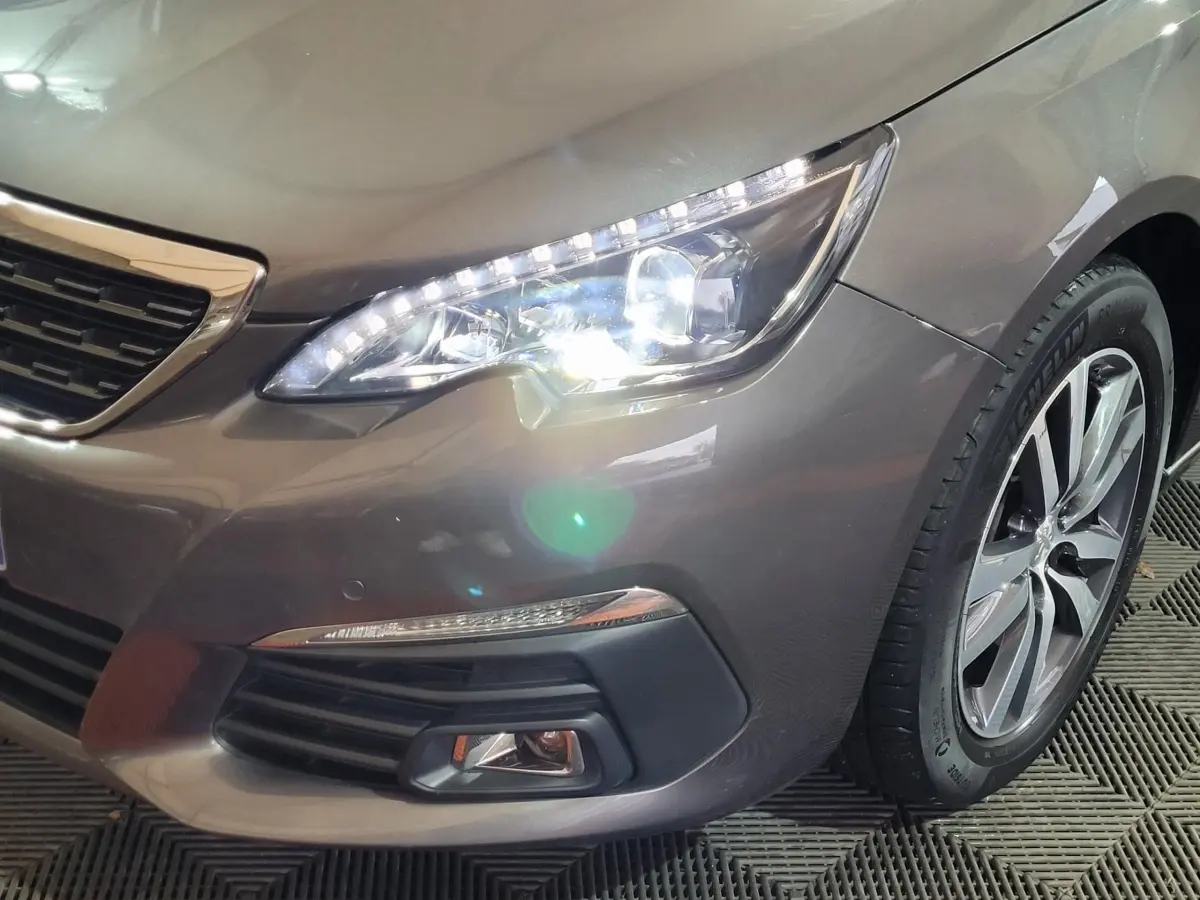 Gros plan sur l'avant droit d'une Peugeot 308 gris foncé, mettant en valeur le phare LED et la roue alliage.