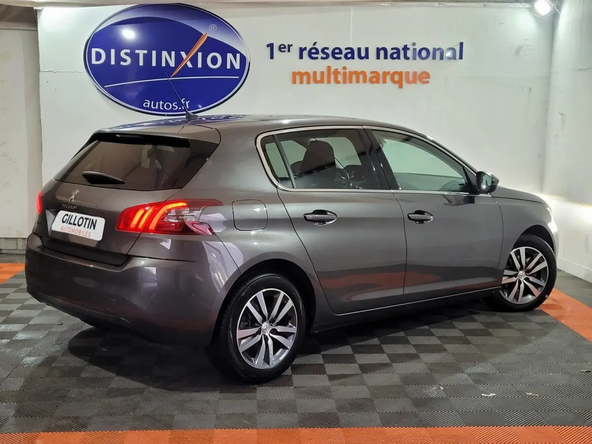 Peugeot 308 gris foncé vue de profil côté droit, feux arrière allumés dans un garage multimarque.