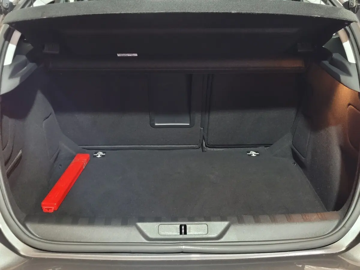 Coffre ouvert d'une Peugeot 308 gris foncé, montrant l'espace de chargement avec un triangle de signalisation rouge à gauche.