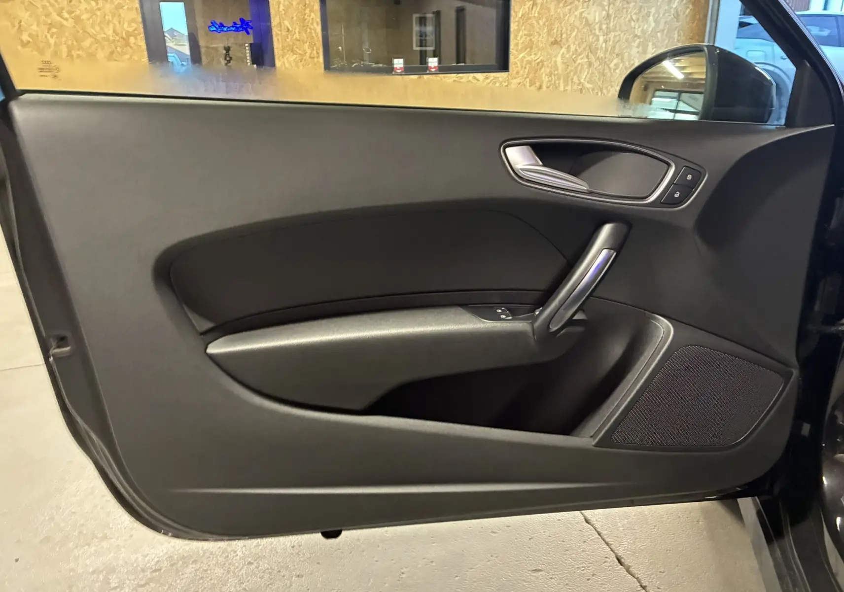 Vue intérieure de la porte côté conducteur noire de l'Audi A1 1.0 TFSI S-Line avec poignée argentée et haut-parleur intégré.