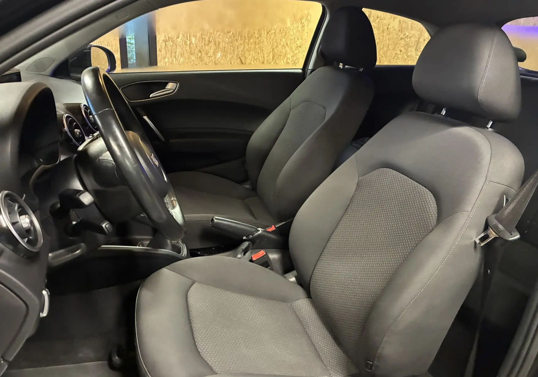 Vue intérieure côté conducteur de l’Audi A1 2016 noire, mettant en valeur les sièges tissu gris-noir et le volant.