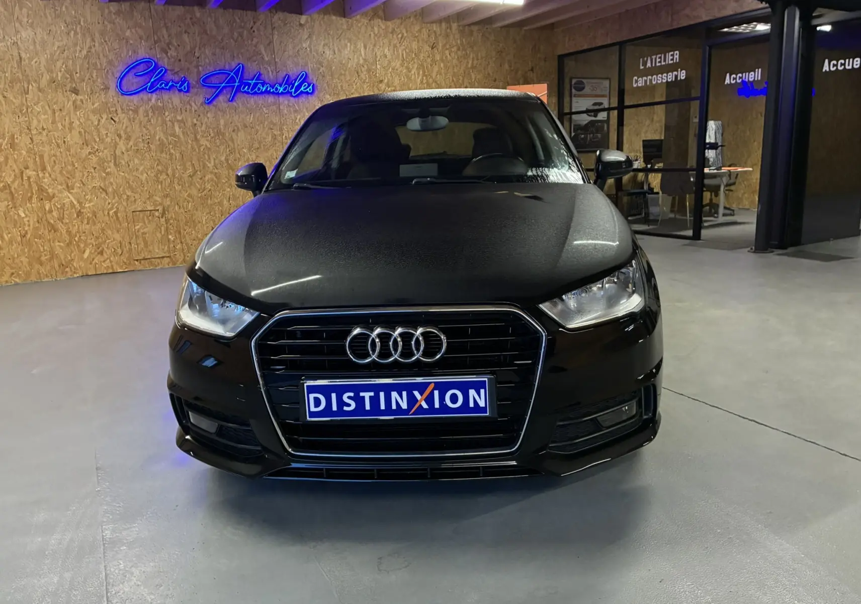 Vue de face d'une Audi A1 noire 2016 avec calandre chromée et logo quatre anneaux, dans un showroom intérieur.