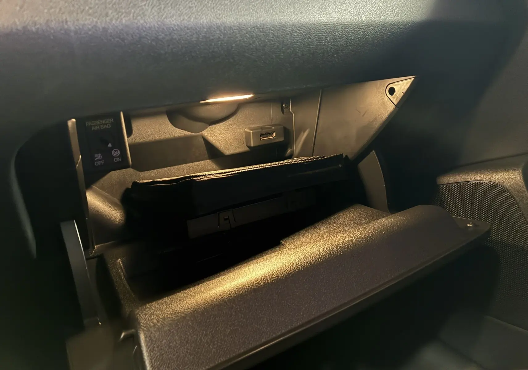 Gros plan de la boîte à gants ouverte de l'Audi A1 noire, avec éclairage intérieur et prise USB visible.
