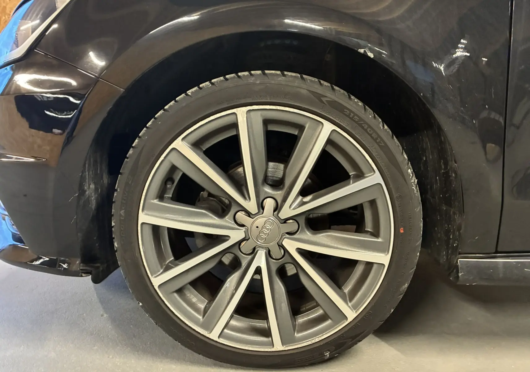 Gros plan sur la roue avant droite d’une Audi A1 noire de 2016 avec jante alliage S-Line à dix branches.