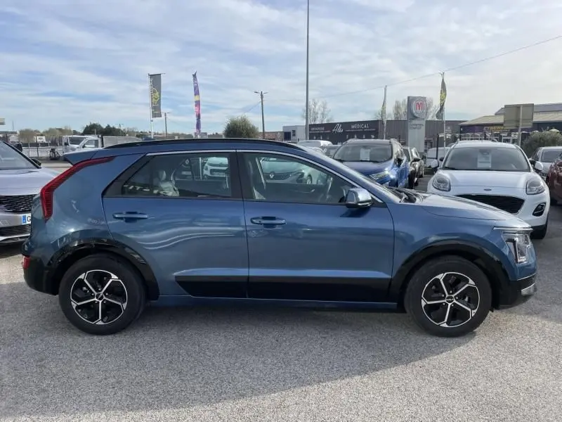 Vue de profil côté gauche d’un KIA NIRO 2024 bleu métal avec jantes alliage et détails noirs sur les bas de caisse.