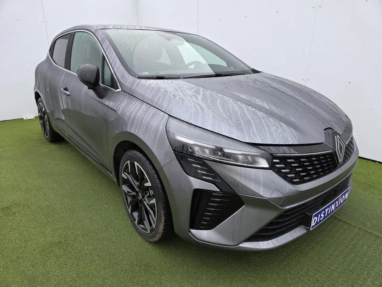 Renault Clio V gris schiste métal vue 3/4 avant gauche avec jantes alliage noires et phares LED distinctifs.