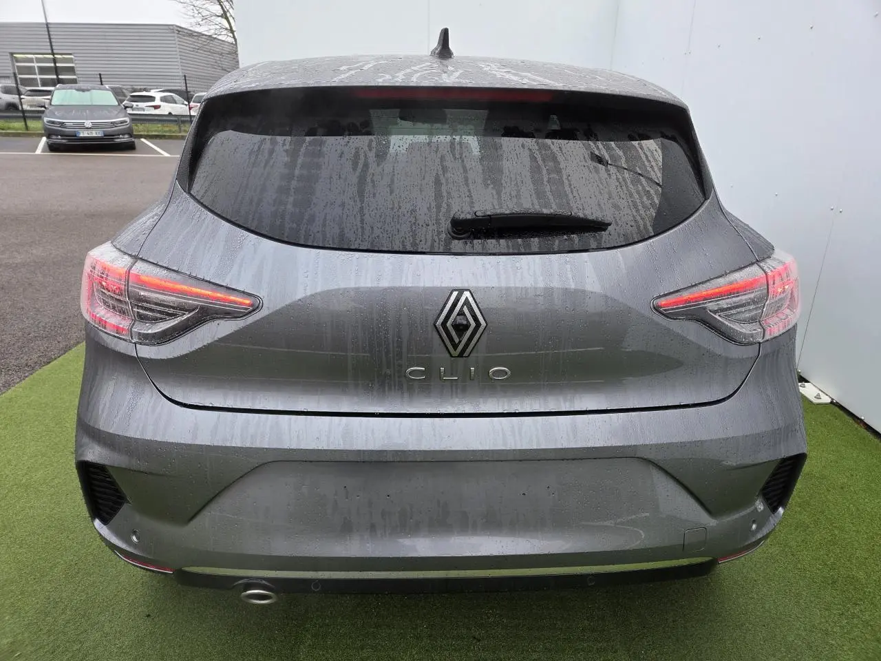 Vue arrière d'une Renault Clio gris schiste métal 2025 avec feux LED et vitre arrière surteintée sous la pluie.
