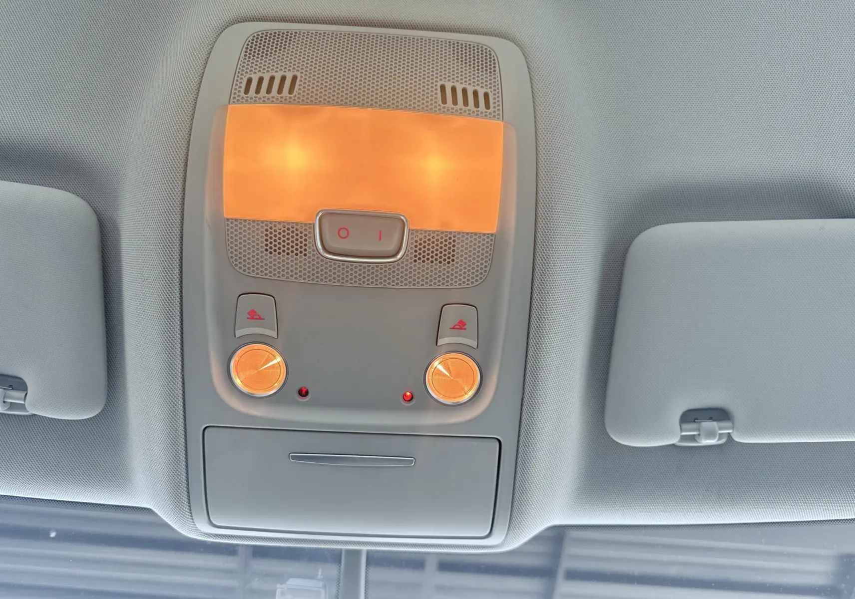 Plafonnier intérieur allumé vu de dessous dans un Audi Q5 noir, avec deux boutons et deux lampes rondes orangées.