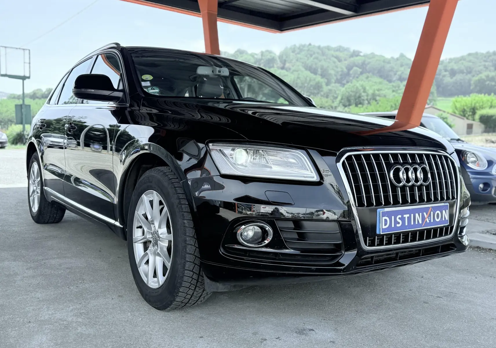Audi Q5 noir vue 3/4 avant droit sous abri, mettant en valeur sa calandre chromée et ses jantes argentées.