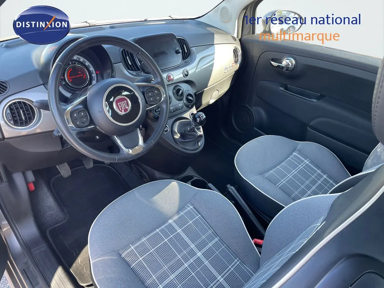 Intérieur clair de la Fiat 500C 2019, vue côté conducteur, avec tableau de bord gris métallisé et sièges tissu gris à motifs.