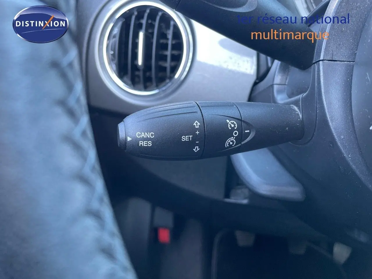 Gros plan sur la commande de régulateur de vitesse à gauche du volant dans l'habitacle d'une Fiat 500C grise.