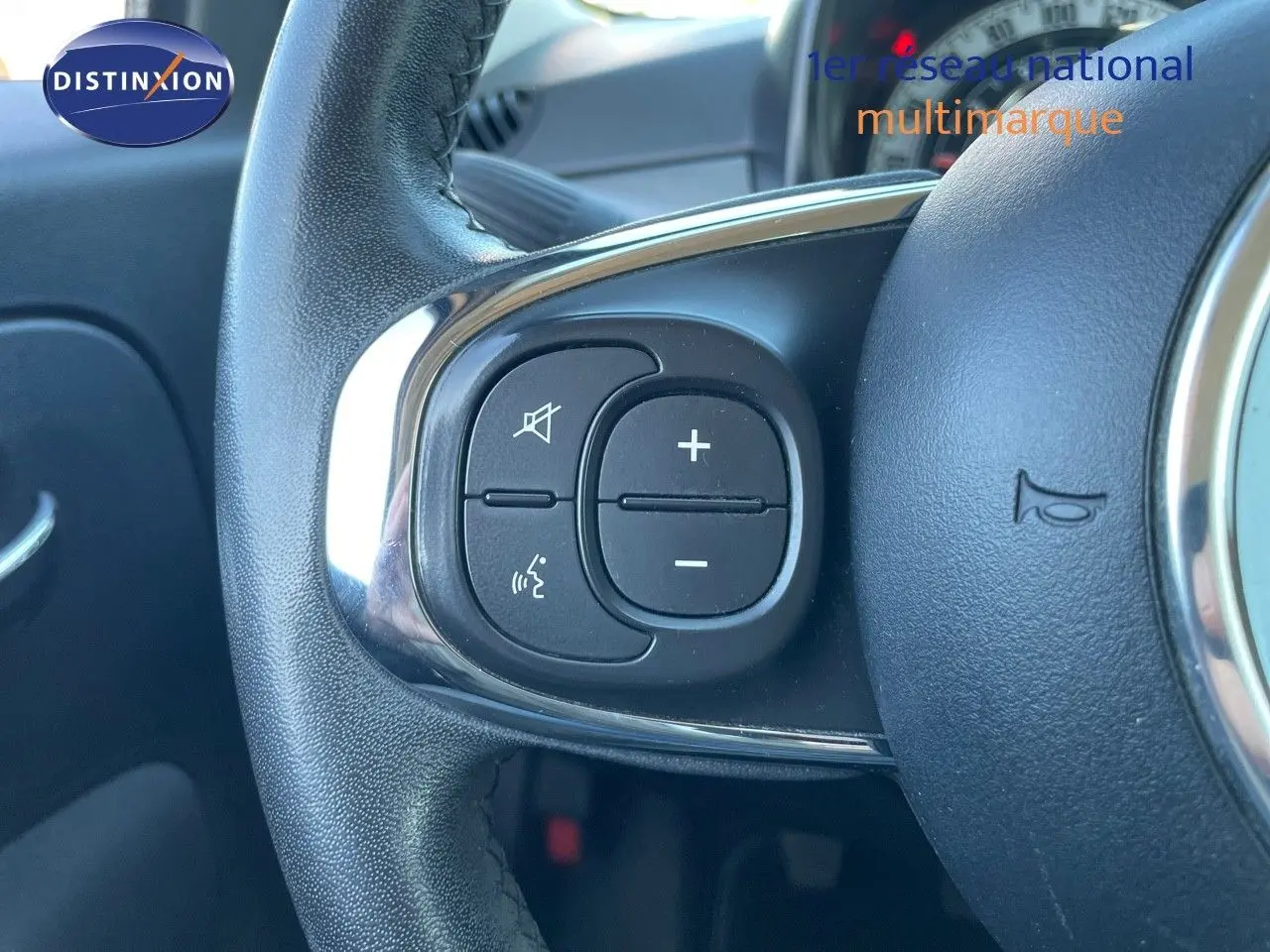 Gros plan sur les commandes de volume et de son du volant d'une FIAT 500C grise électroclash, intérieur visible en arrière-plan.