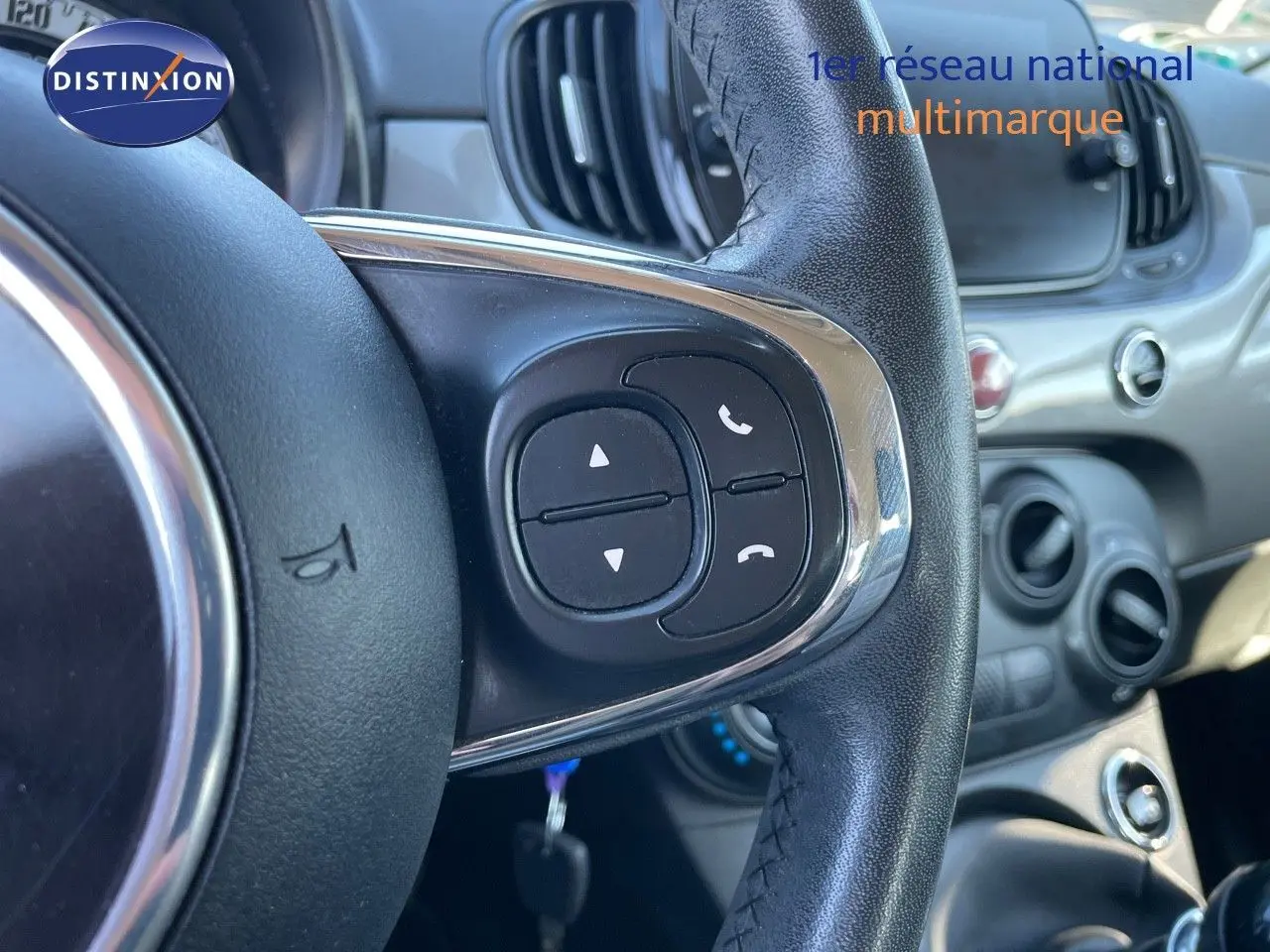 Gros plan sur le volant noir de la Fiat 500C 2019 avec commandes intégrées, tableau de bord gris métallisé en arrière-plan.