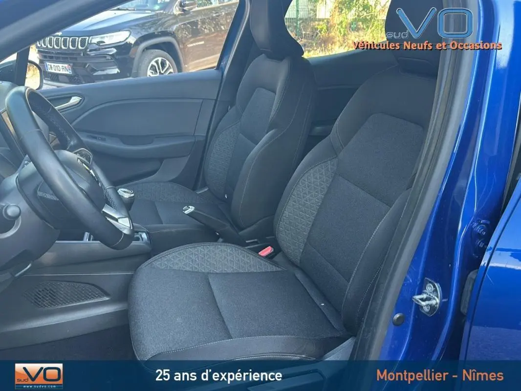Vue intérieure côté conducteur d'une Renault Clio bleu foncé 2023 avec sièges tissu noirs et boîte manuelle.