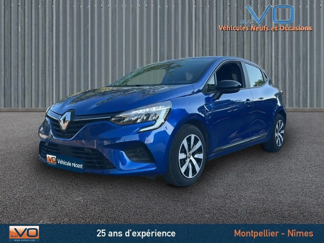 Renault Clio V TCe 90 Equilibre bleu foncé vue 3/4 avant droit sur sol gris devant un mur métallique.