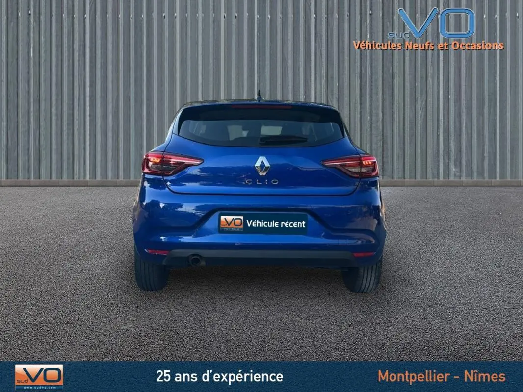 Vue arrière d'une Renault Clio bleu foncé 2023, avec feux arrière allumés sur un sol goudronné.
