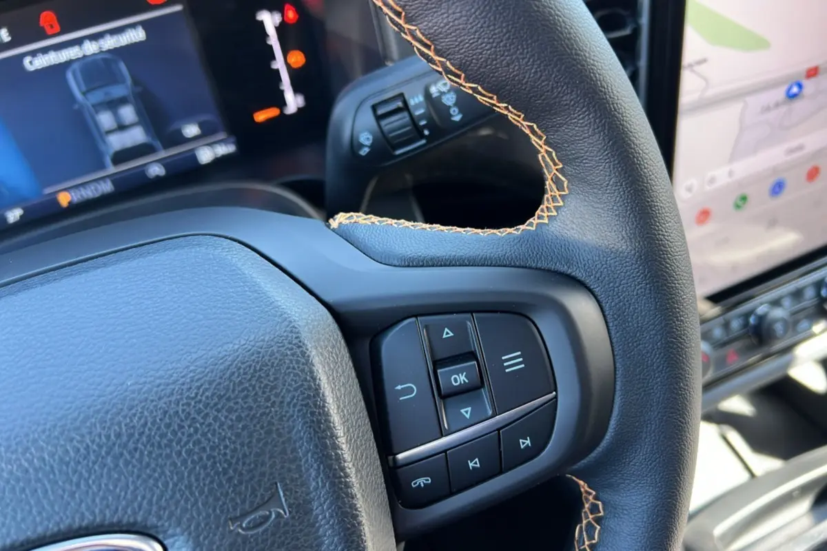 Gros plan sur le volant cuir noir avec surpiqûres orange et commandes multifonctions du Ford Ranger Wildtrak 2025.