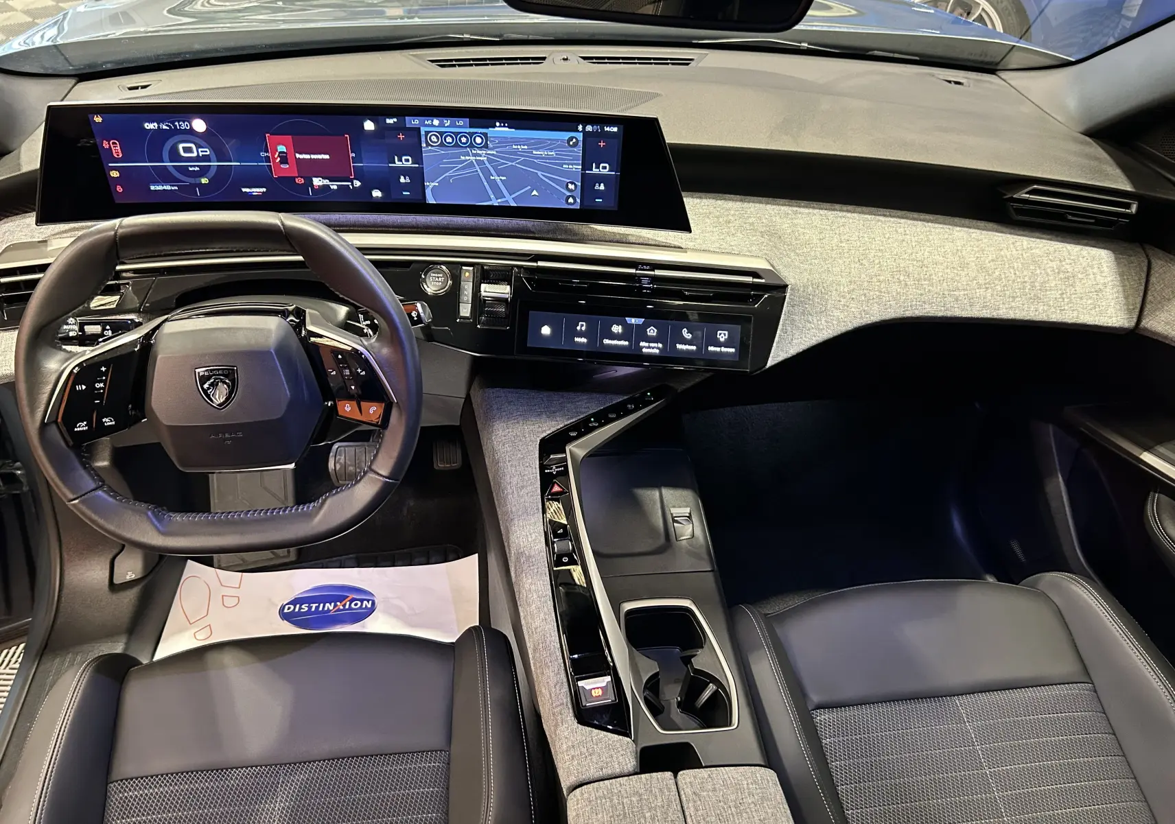 Vue intérieure du tableau de bord et volant du Peugeot 3008 Hybrid 2024 avec finition tissu et écran panoramique i-Cockpit.