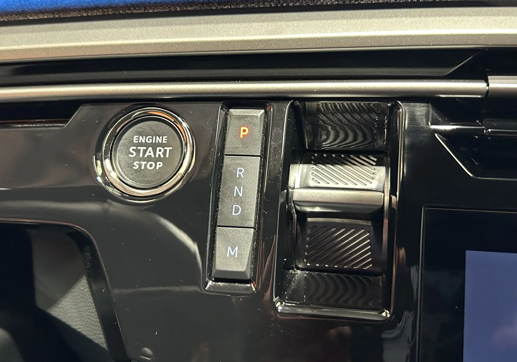 Gros plan sur la console centrale noire brillante du Peugeot 3008 III Hybrid avec bouton start/stop et commandes de boîte auto.