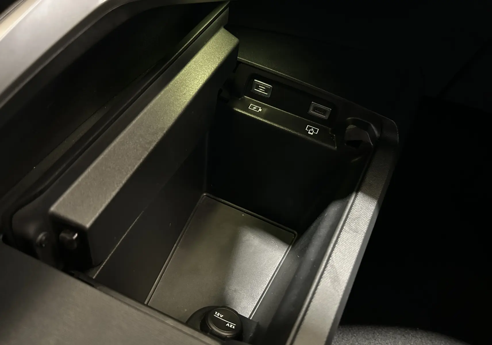 Vue rapprochée de la console centrale noire du Peugeot 3008 Hybrid 2024 avec prises USB et prise 12V visibles.