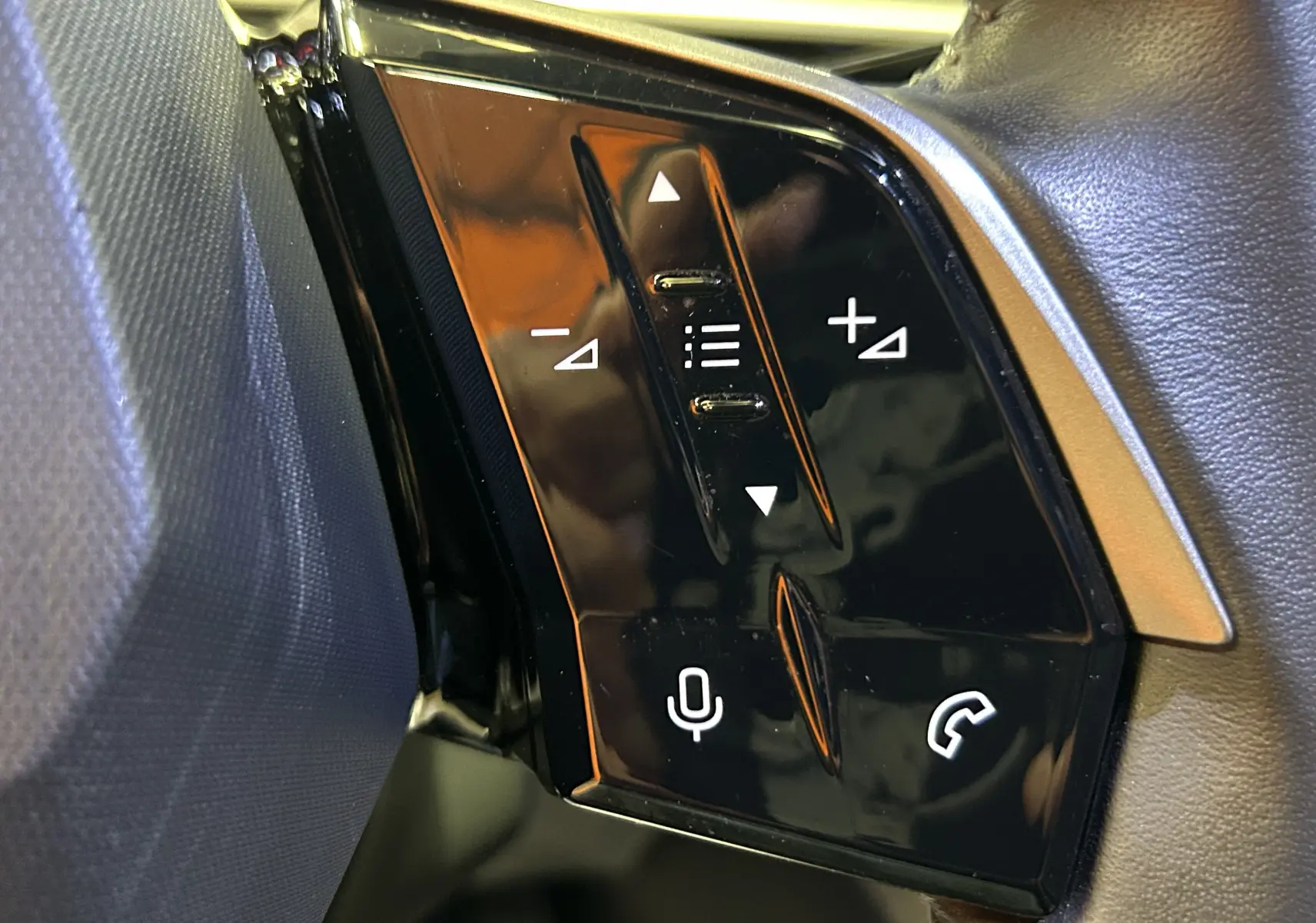 Gros plan sur les commandes noires brillantes du volant côté gauche du Peugeot 3008 bleu Ingaro 2024.