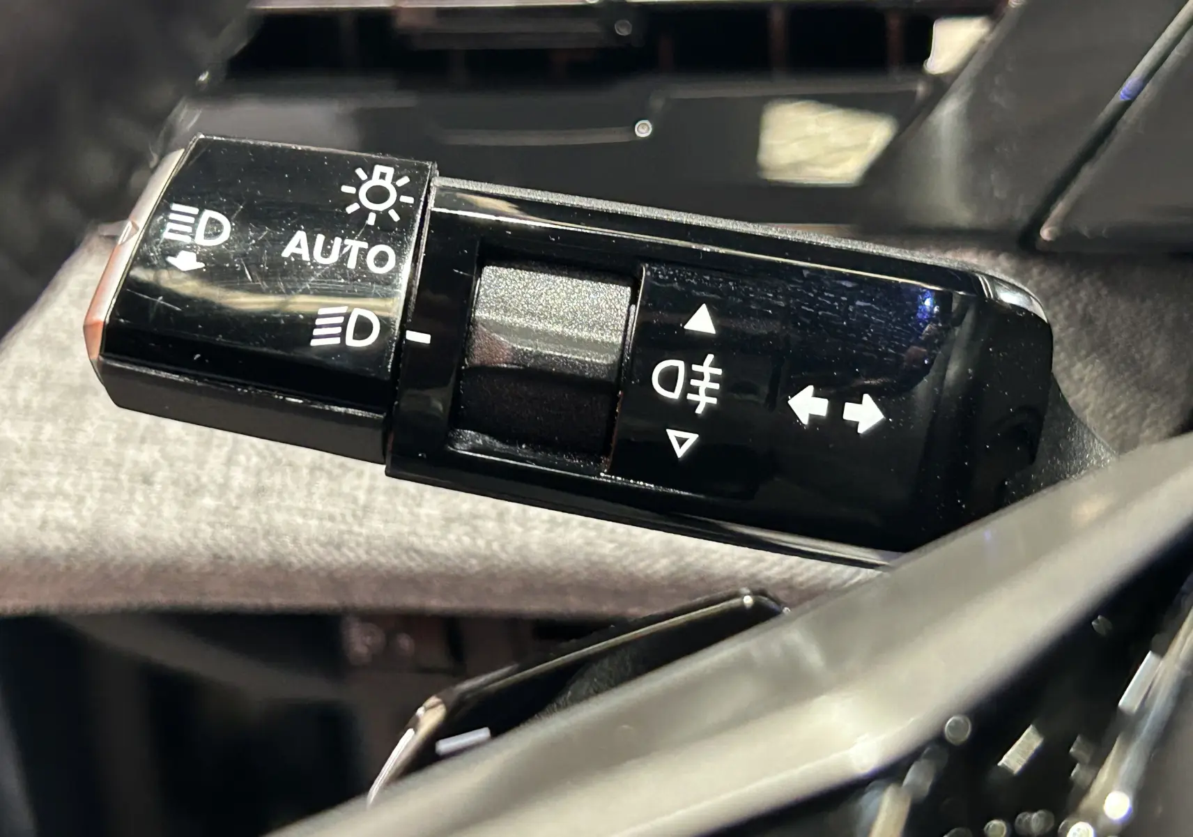 Gros plan sur la commande des feux et clignotants du Peugeot 3008 Hybrid 2024, finition noire brillante.