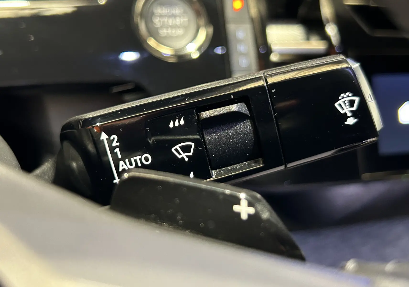 Gros plan sur la commande d’essuie-glace noir du Peugeot 3008 Hybrid 2024, avec bouton start visible en arrière-plan.